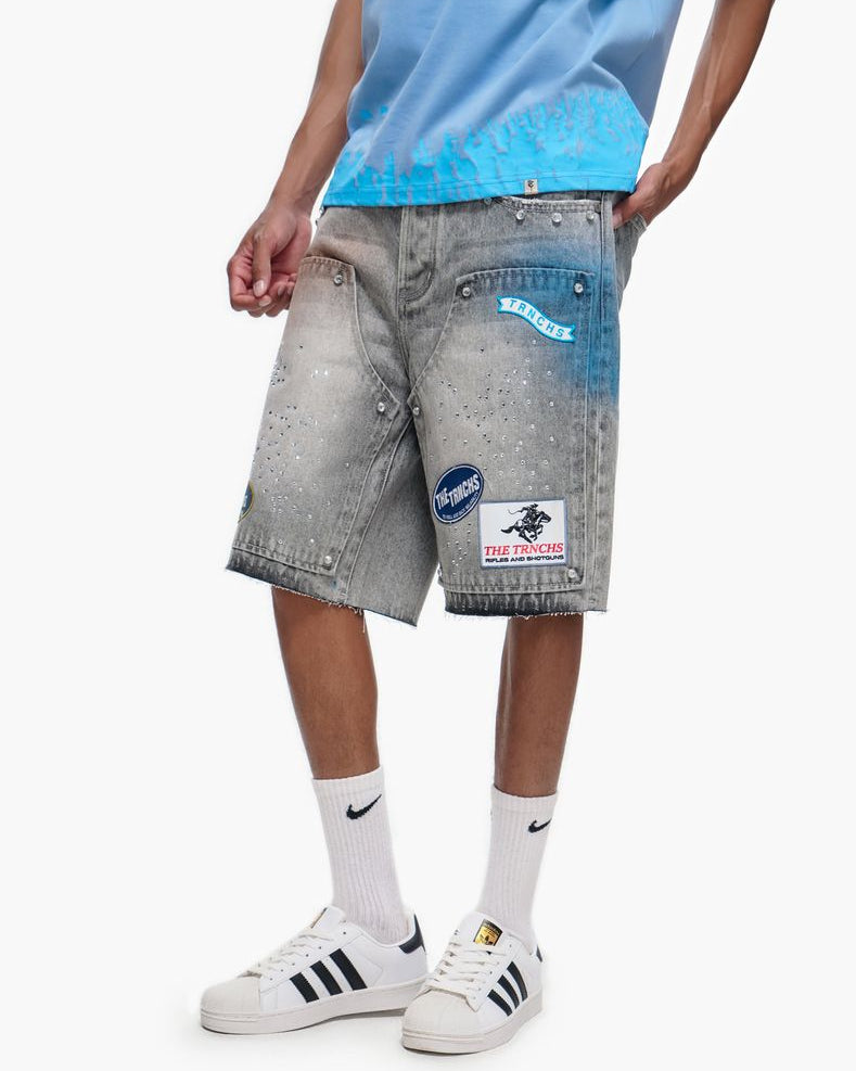 Person wearing gray denim shorts with patches and a blue shirt on a white background