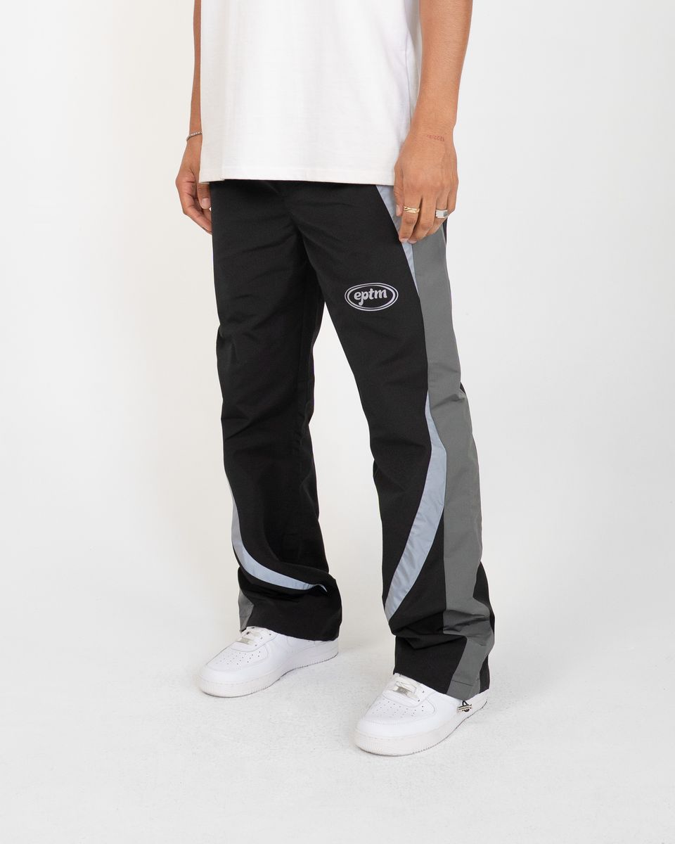 Person wearing black and gray track pants with a logo on a white background