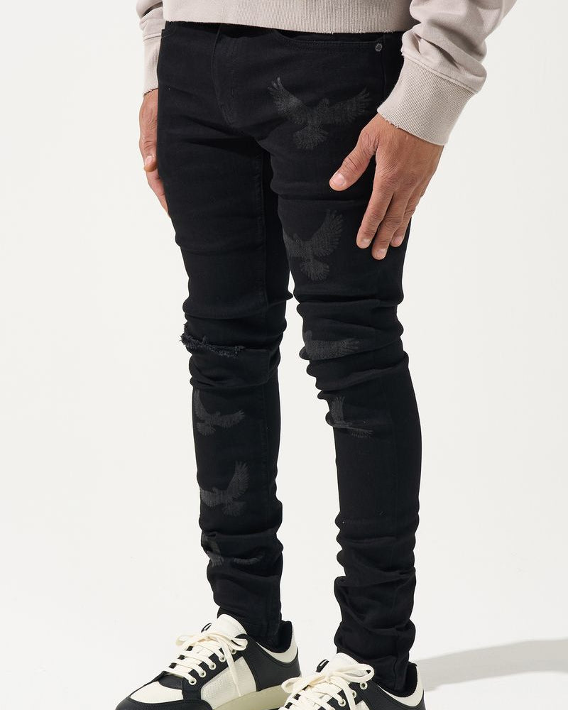 Person wearing black distressed jeans and black and white sneakers on a light gray background