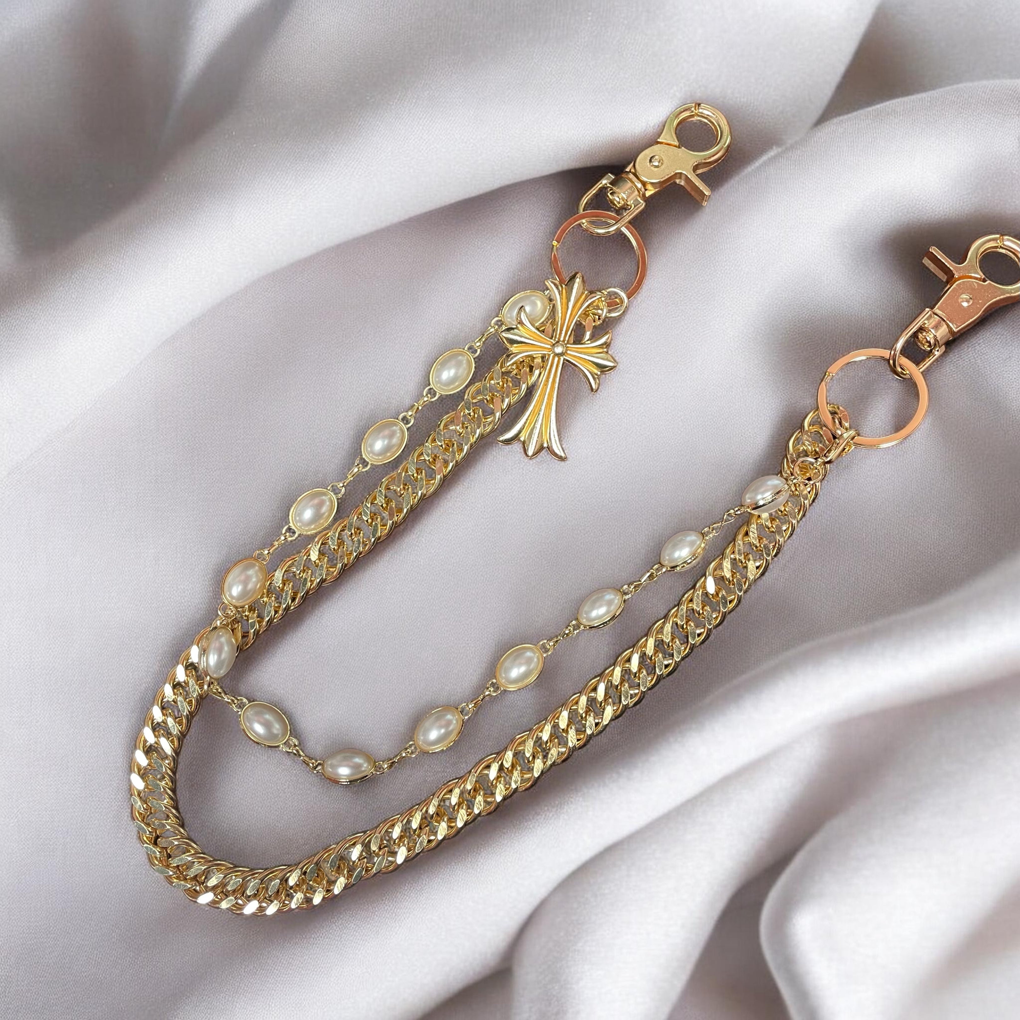 Gold chain with pearls and a cross pendant on a white fabric background
