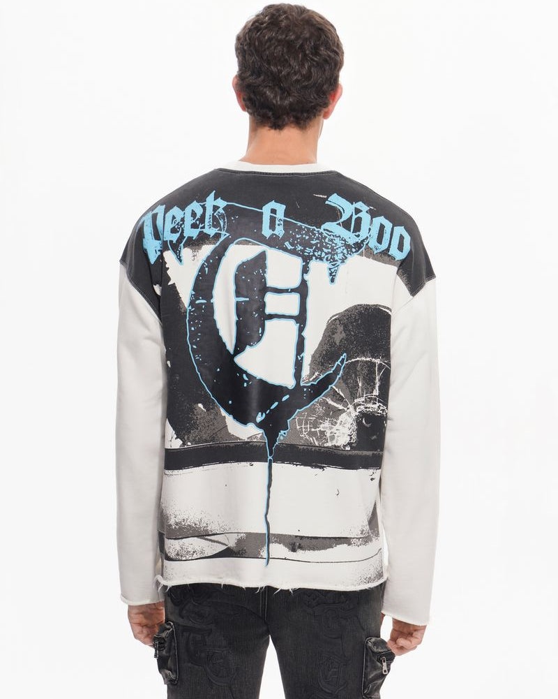 Person wearing a white sweatshirt with black and blue graphics on the back, standing against a white background.