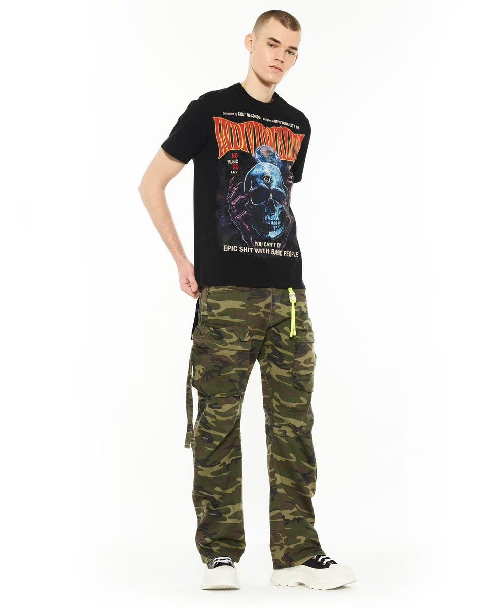 Person wearing a black t-shirt with graphic design and green camouflage pants on a white background