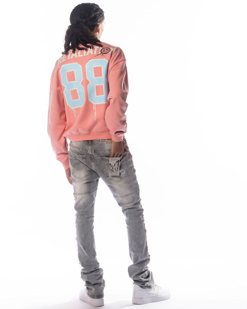 Person wearing a pink sweatshirt with blue numbers and gray jeans on a white background