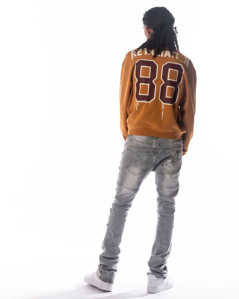 Person wearing a brown varsity jacket with 'Fellatio' printed on the back, standing against a white background.
