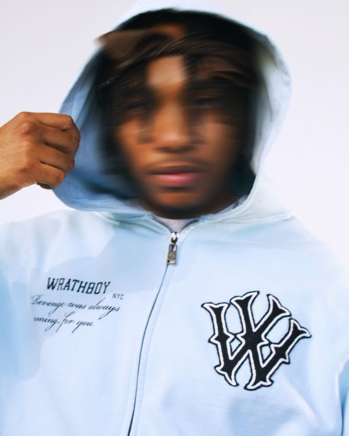 Person wearing a light blue hoodie with logos and text, against a plain background