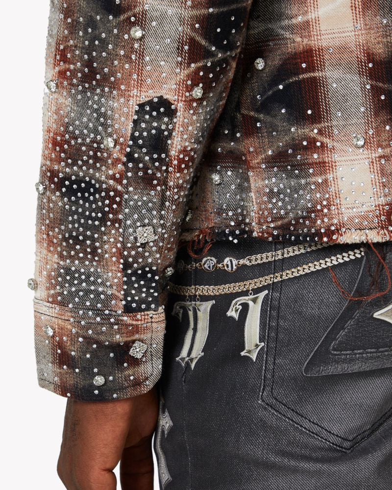 Close-up of a person wearing a plaid shirt with embellishments and dark jeans.