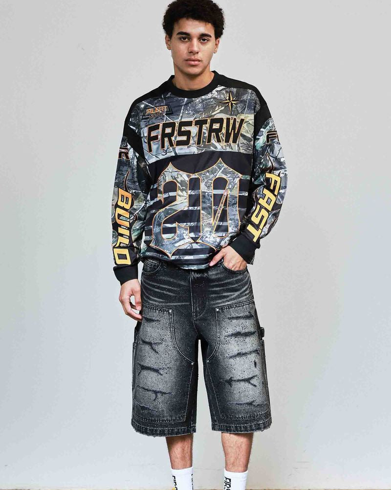 Person wearing a patterned sweatshirt and denim shorts against a plain background