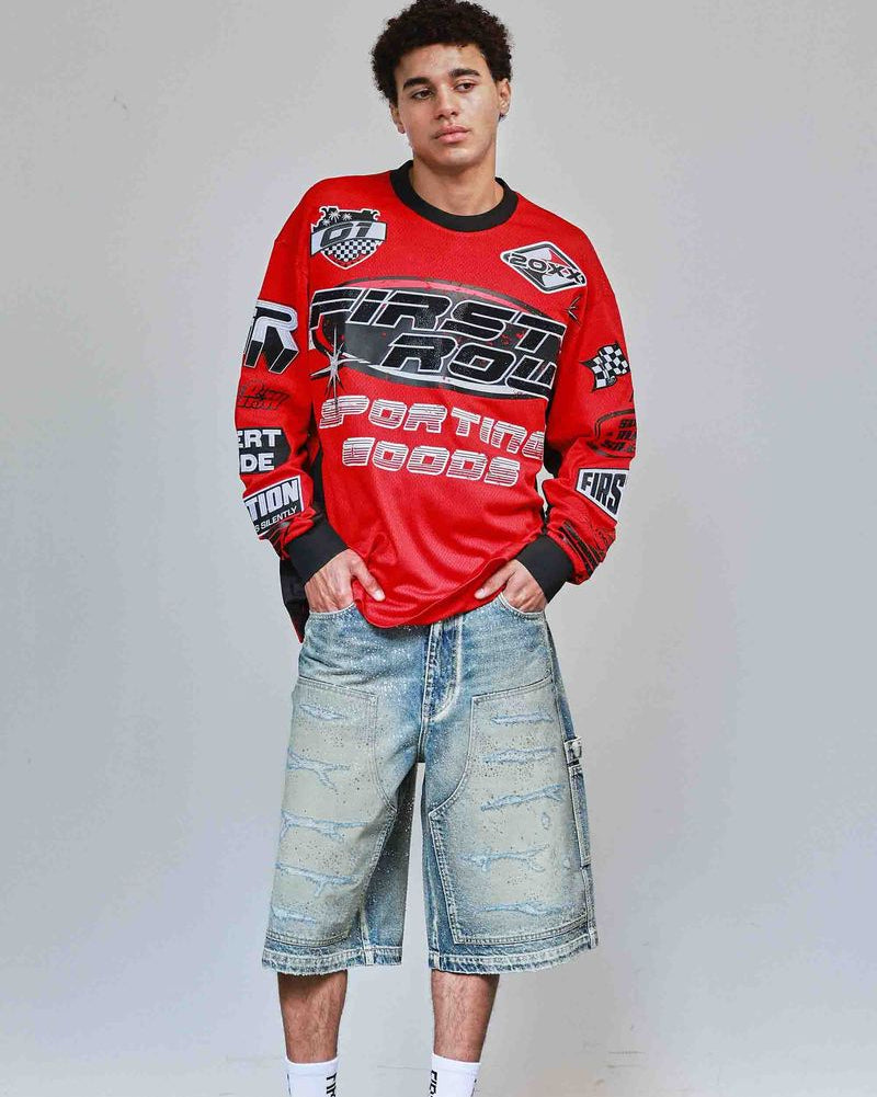 Person wearing a red sweatshirt with branding and denim shorts on a plain background
