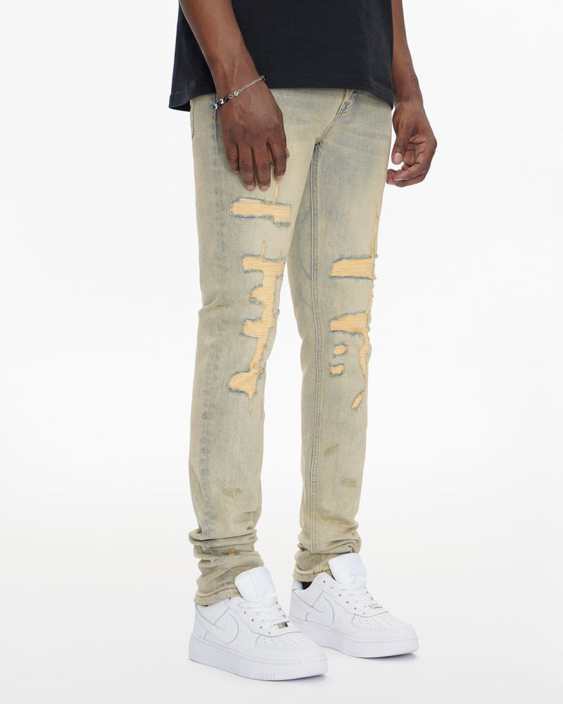 Person wearing light gray distressed jeans with yellow accents on a white background