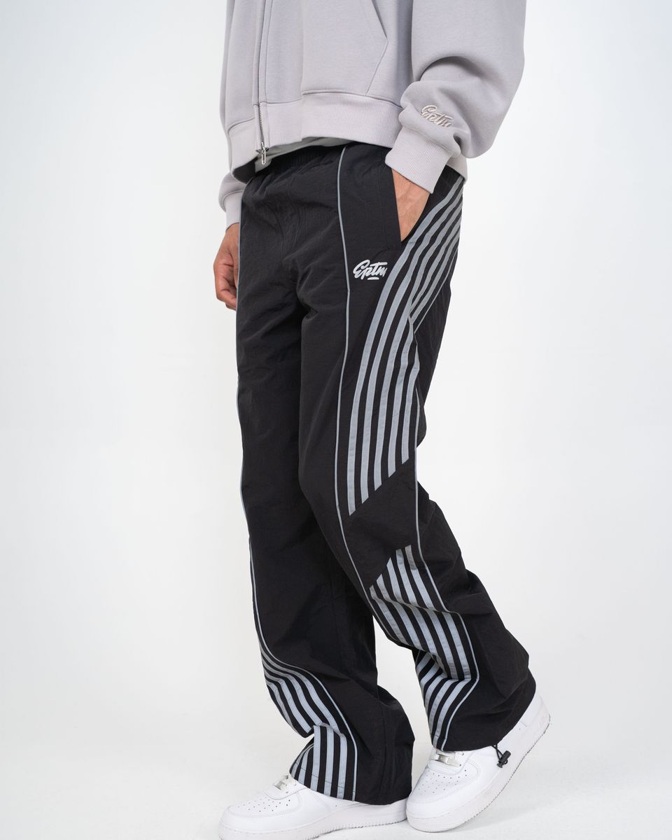 Person wearing black track pants with white stripes and a gray hoodie on a white background