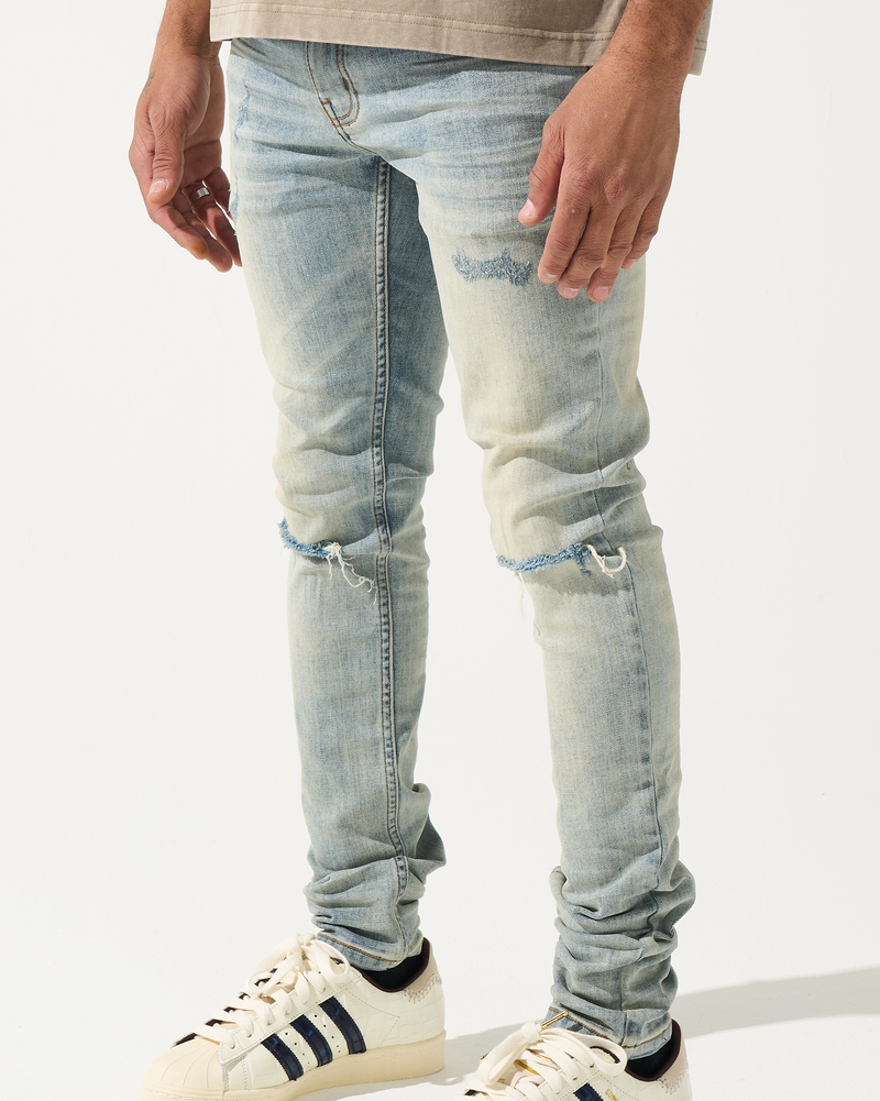 Person wearing light blue ripped jeans and white sneakers with black stripes on a white background