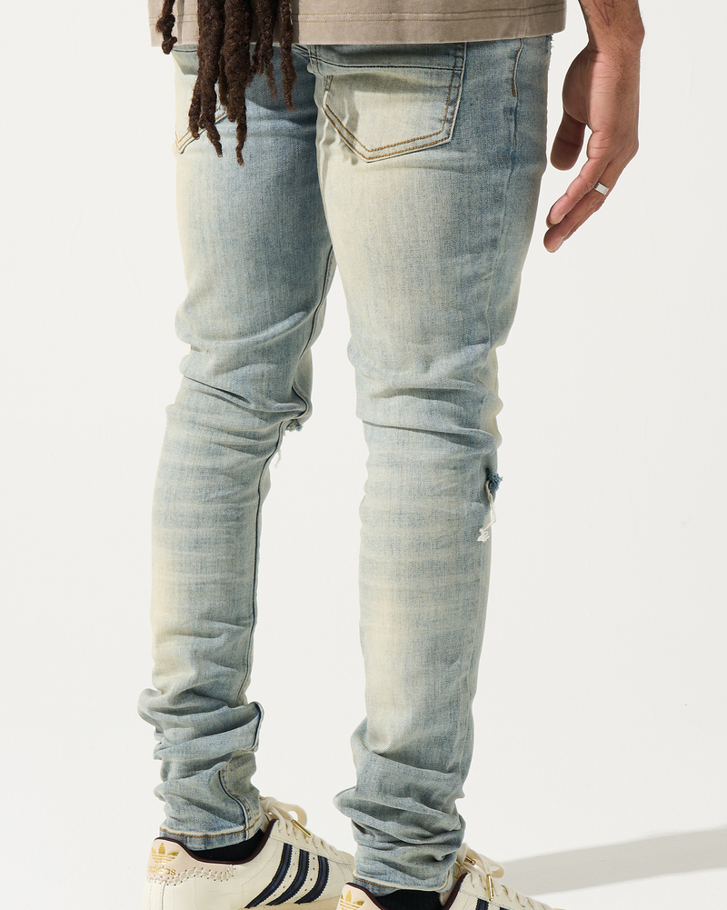 Person wearing light blue jeans and white sneakers with black stripes on a white background