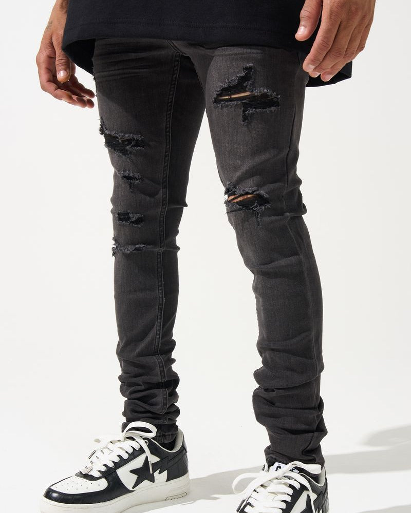 Person wearing black ripped jeans and black and white sneakers on a white background