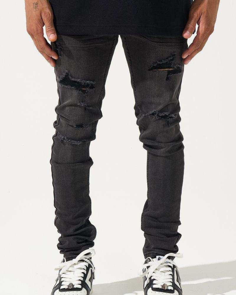 Person wearing black distressed jeans and black and white sneakers on a white background