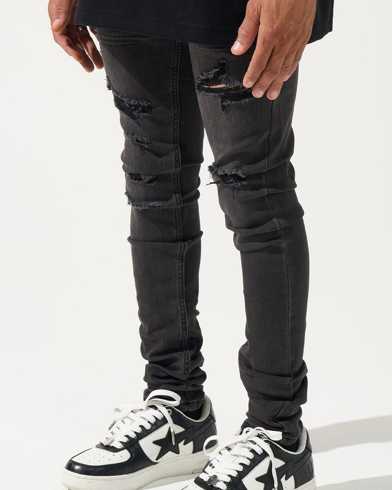 Person wearing black ripped jeans and black and white sneakers on a white background