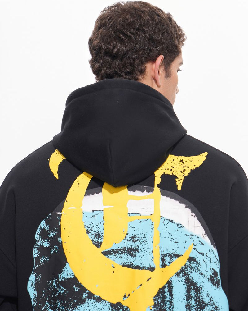 Person wearing a black hoodie with a yellow and blue graphic design on the back against a white background