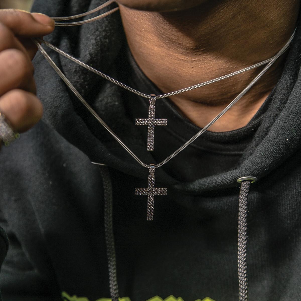 Person wearing a black hoodie with silver chain necklaces with cross pendants.
