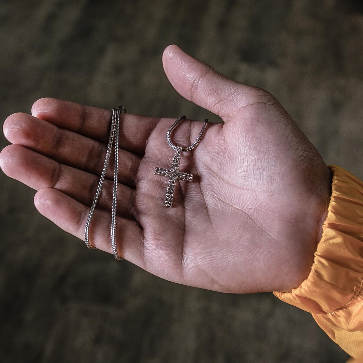Hand holding a silver necklace with a cross pendant against a blurred background