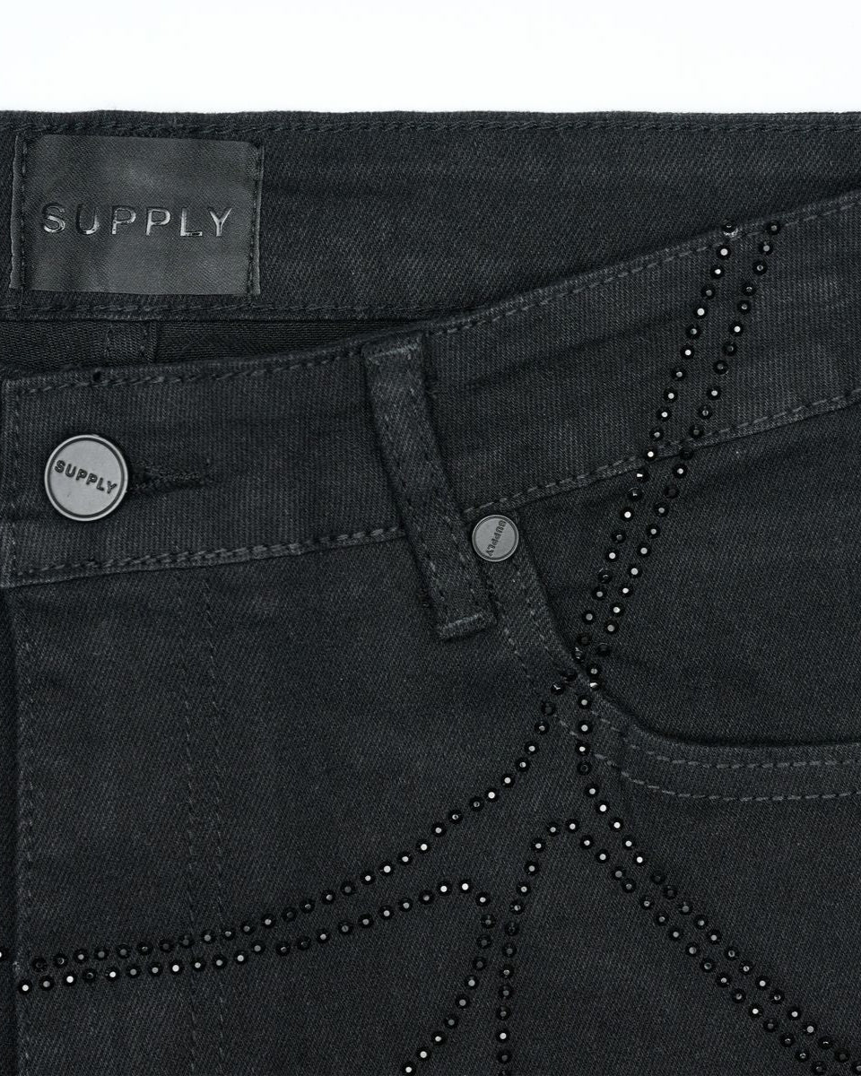Close-up of black pants with 'Supply' label and decorative beads.