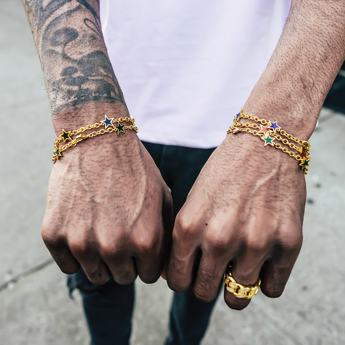 Close-up of hands wearing the gold star cleef bracelets and a ring on a neutral background