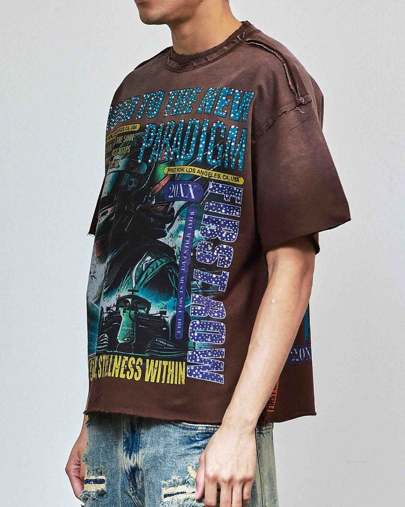 Person wearing a brown graphic t-shirt with a colorful design and ripped jeans on a plain background