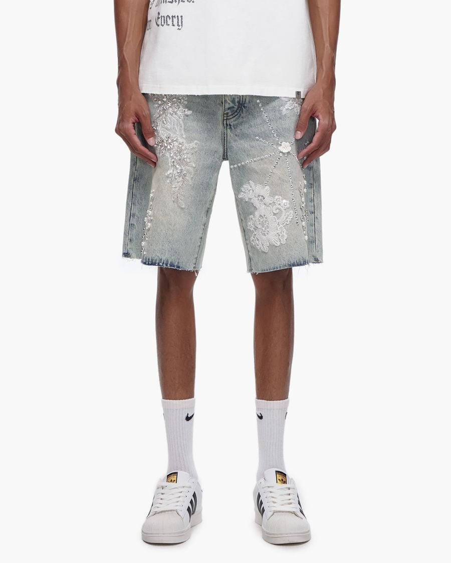 Person wearing light blue denim shorts with white floral patterns on a white background