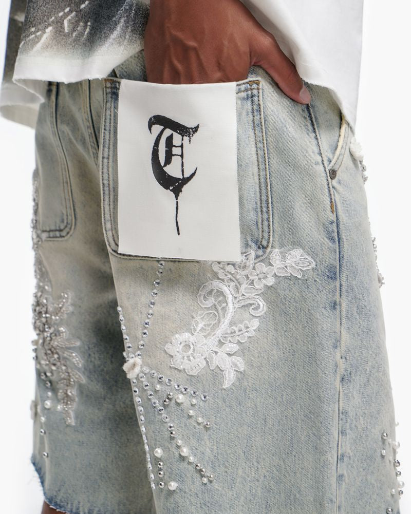 Person wearing a white shirt with text, light blue jeans with lace details, and a white pouch with a black design.