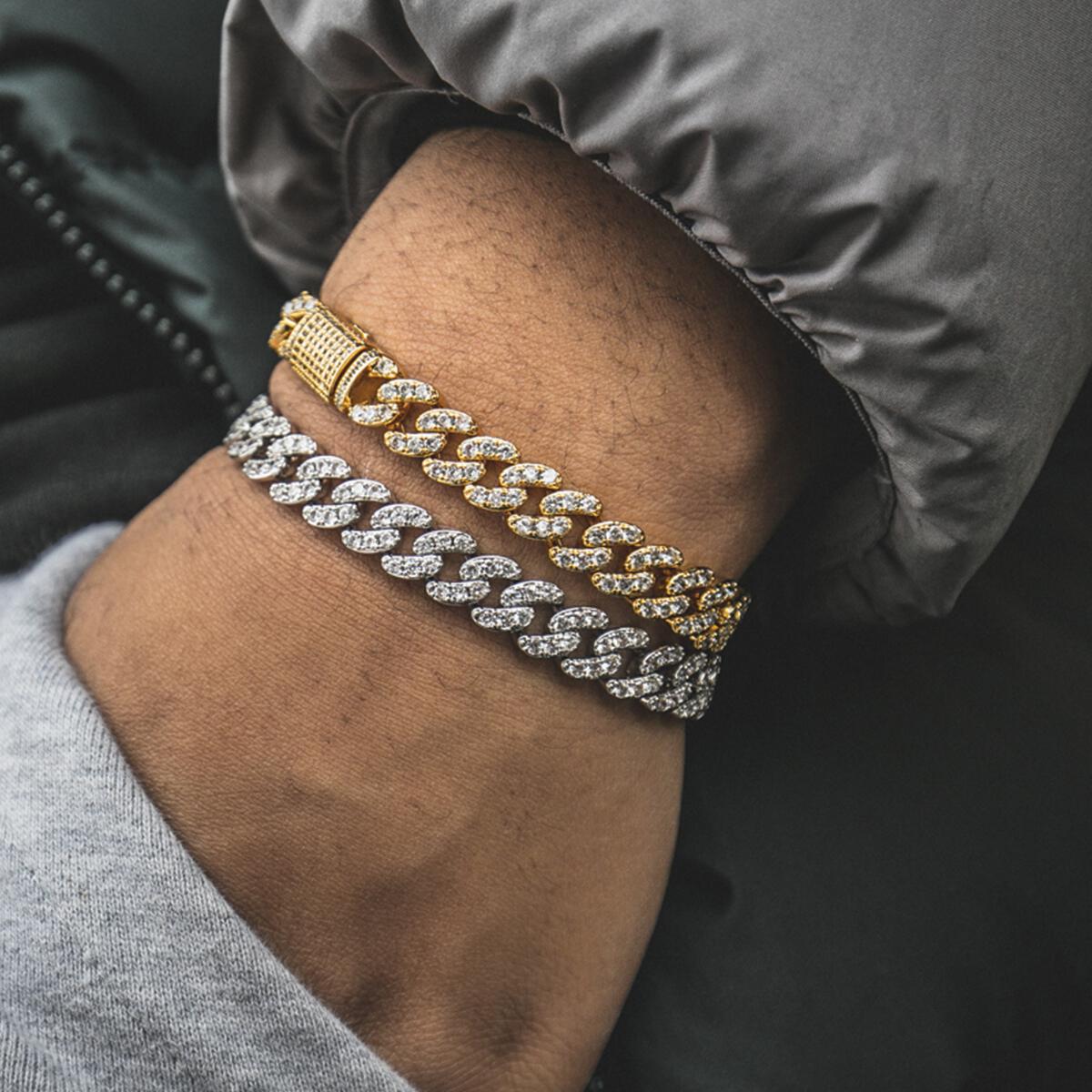 Gold and silver cuban link chain bracelets on a person's wrist with a dark background