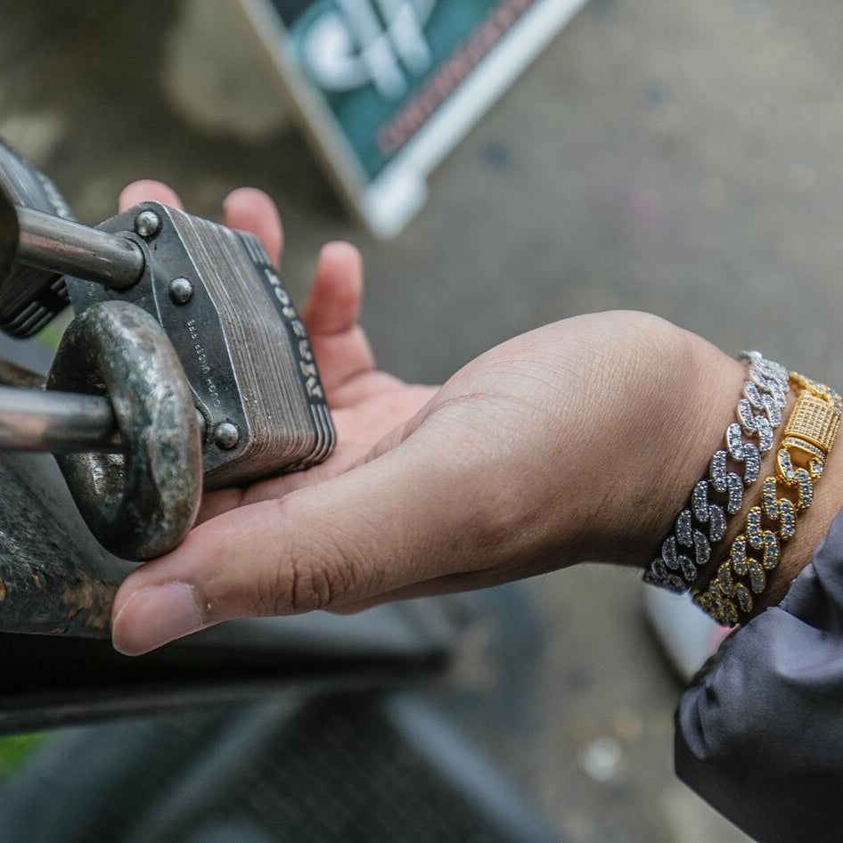 Hand holding a padlock with a focus on jewelry, including a gold and silver Cuban link bracelet.