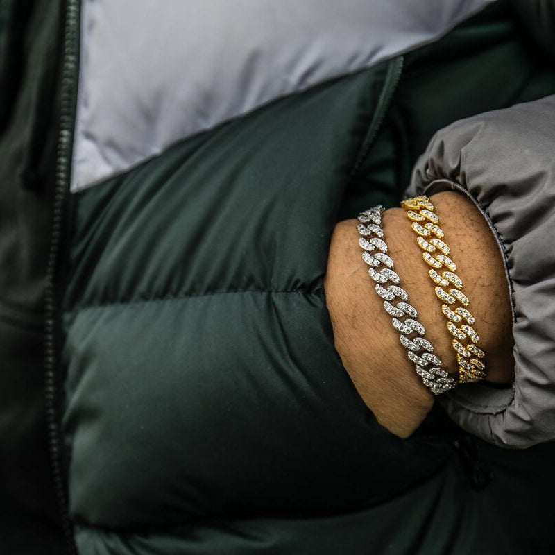 Gold and silver cuban link chain bracelets on a person's wrist with a dark background