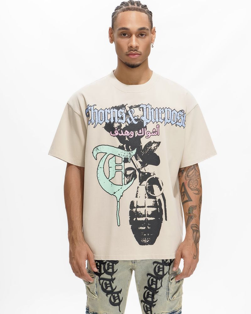 Person wearing a beige t-shirt with graphic design and text, standing against a white background