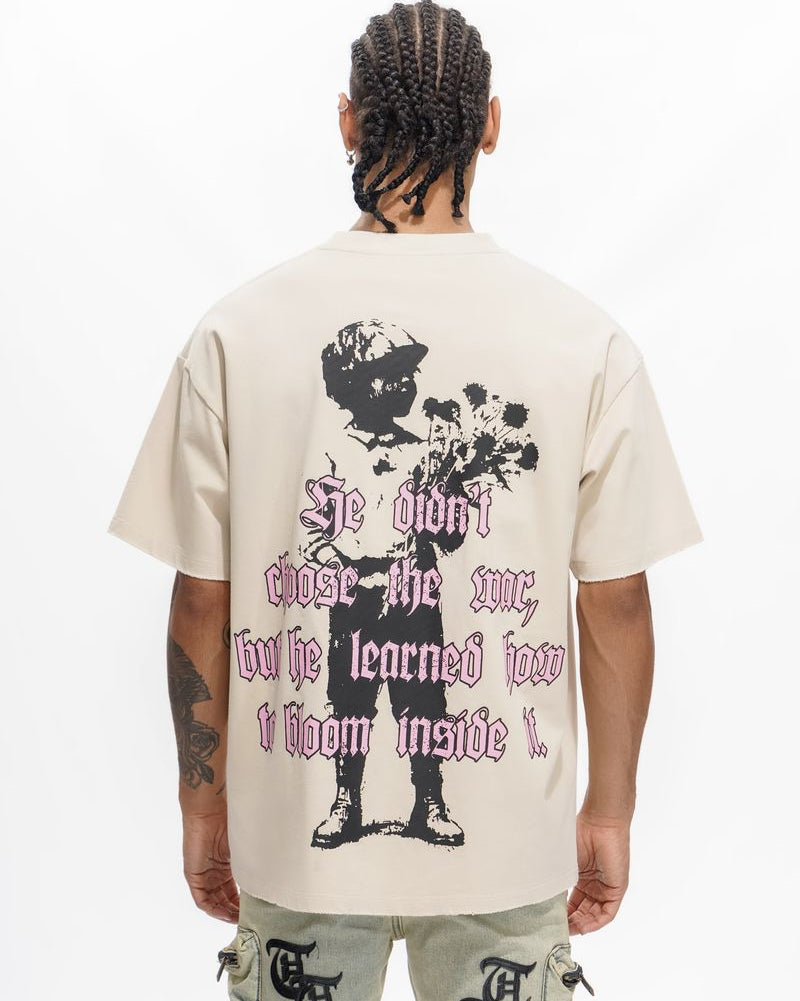 Person wearing a beige t-shirt with a graphic design and text on the back, standing against a white background.