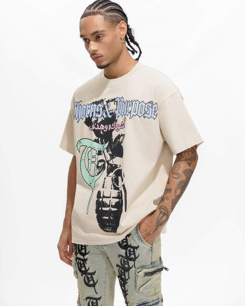 Man wearing a beige graphic t-shirt with tattoos on a white background