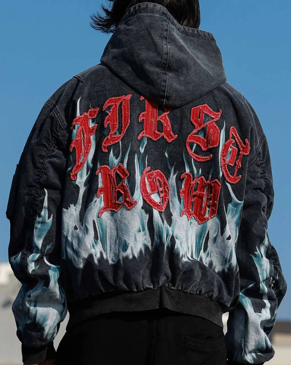 Person wearing a black jacket with red and white text on the back against a clear blue sky.