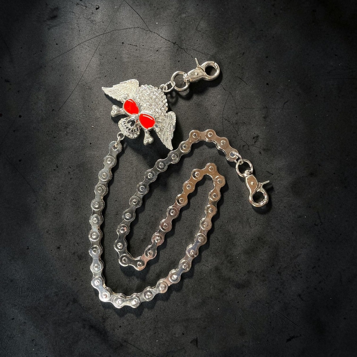 Silver chain with a decorative clasp on a dark textured surface. A WINGED SKULL AS THE MAIN DESIGN.