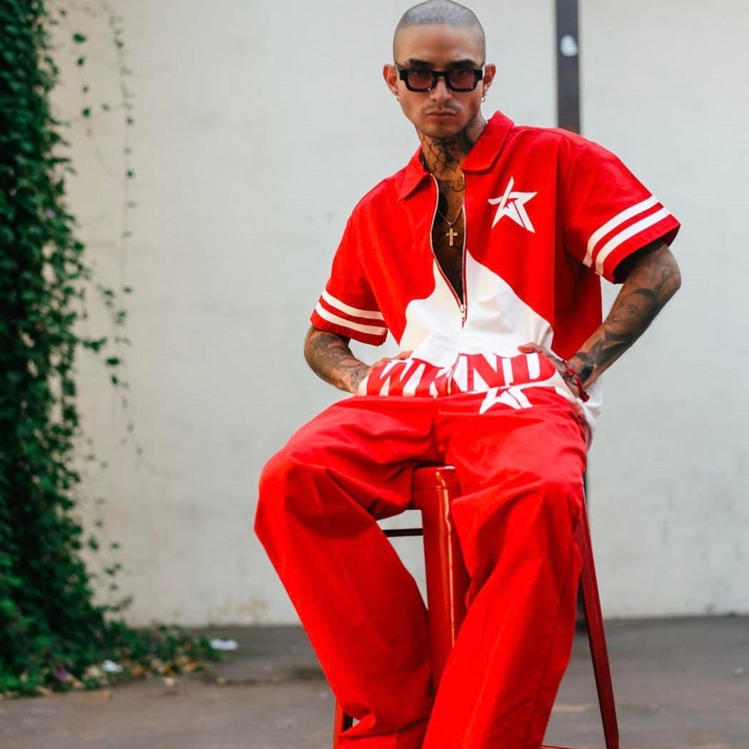 Person wearing a red outfit with a star design, sitting on a stool against a white wall.