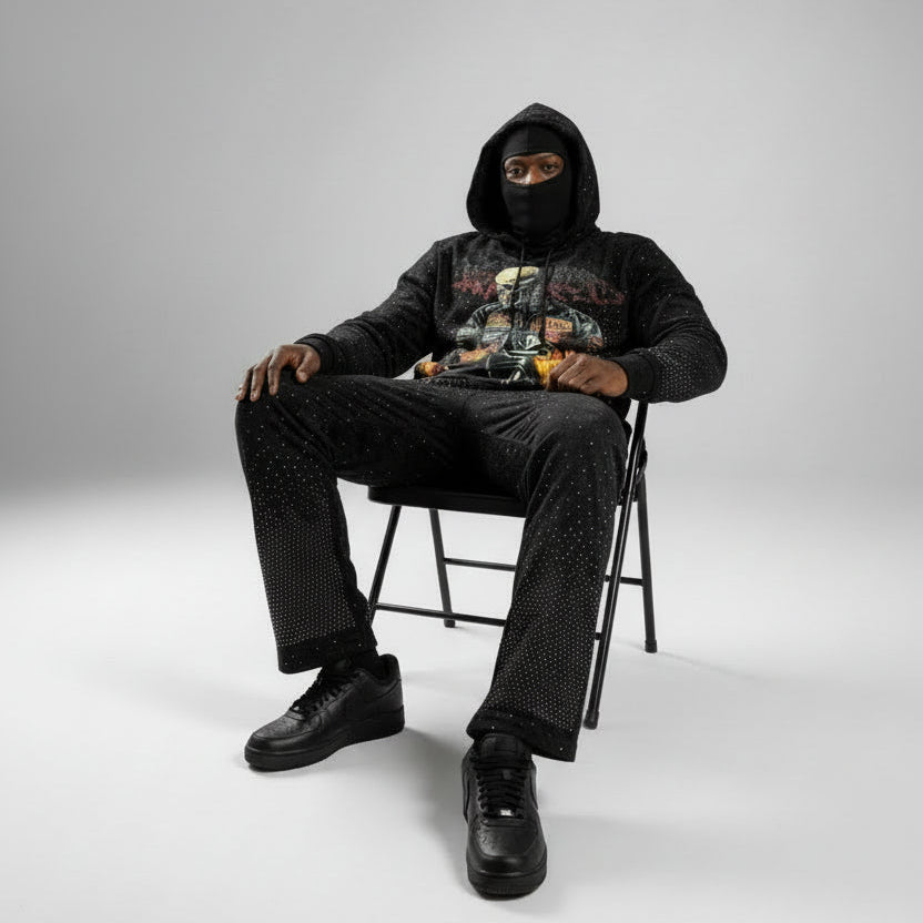Person wearing a black hoodie and pants sitting on a chair against a white background
