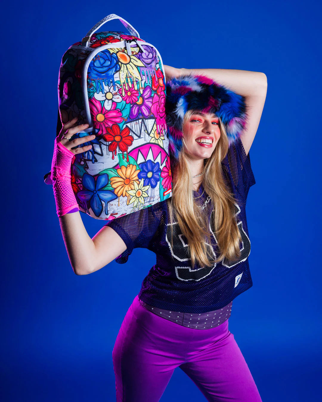 Person holding a colorful floral-patterned backpack against a blue background