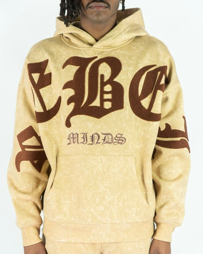 Beige hoodie with brown text worn by a person on a white background