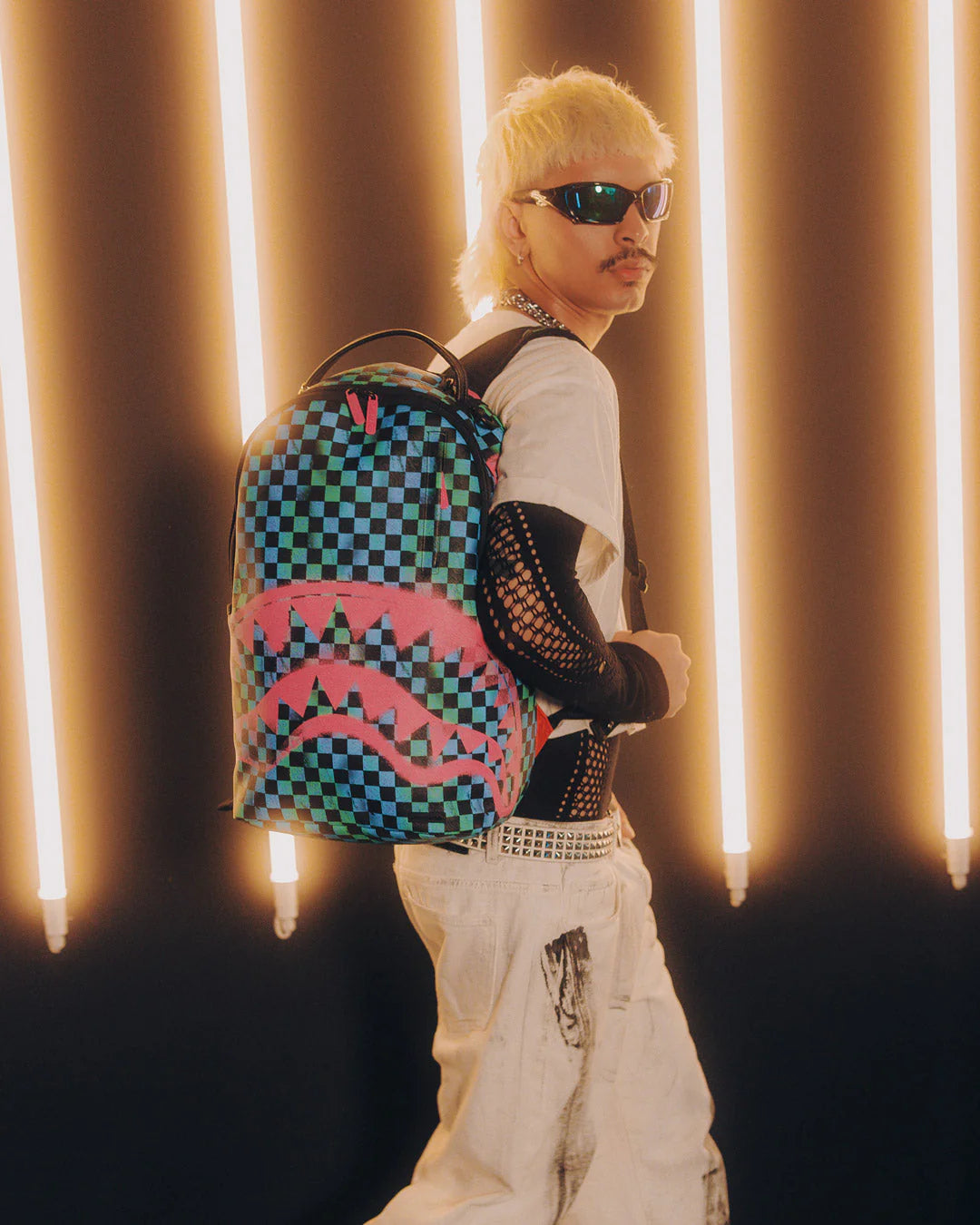 Person wearing a colorful backpack with a checkered design against a curtain background