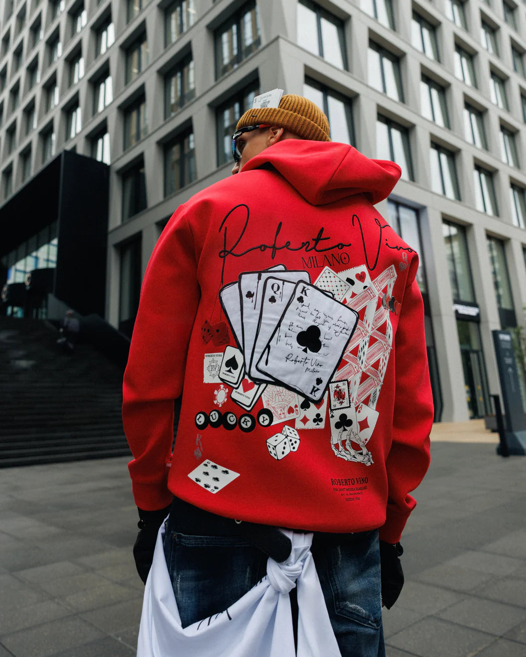 Person wearing a red hoodie with card design in an urban setting