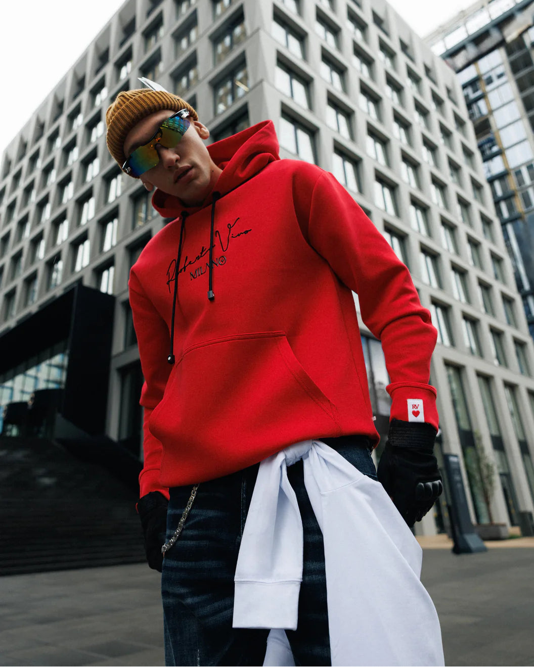Person wearing a red hoodie with a brand logo, standing in an urban setting.
