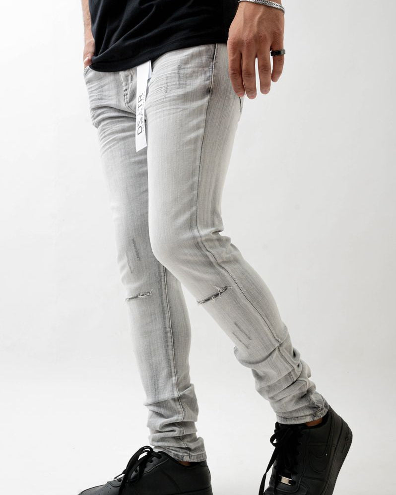 Person wearing light gray distressed jeans and black shoes on a white background