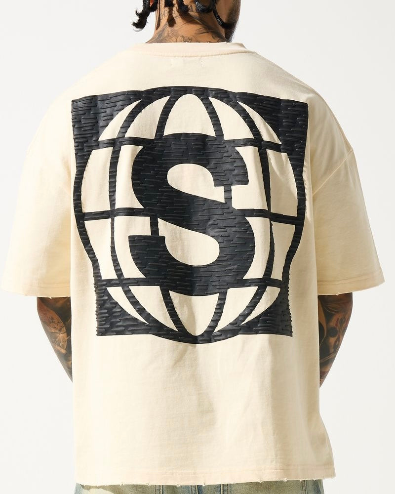 A person wearing a beige crew neck t-shirt with a large 'S' logo on the back, and distressed detailing on the neck and sleeves.