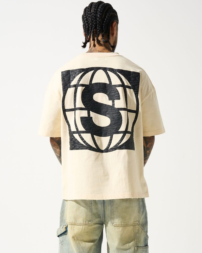 A male model wearing a beige crew neck t-shirt with short sleeves and distressed detailing at the neck and sleeves. The t-shirt has a crew neckline and a slightly cropped fit.