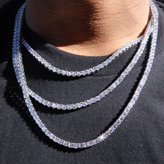 Close-up of a person wearing multiple diamond tennis necklaces on a blurred street background