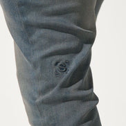 Close-up of dark gray pants with a visible brand logo on a light gray background