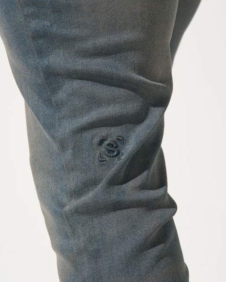 Close-up of dark gray pants with a visible brand logo on a light gray background