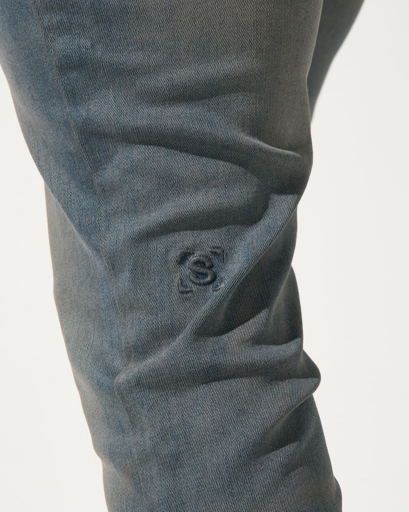 Close-up of dark gray pants with a visible brand logo on a light gray background