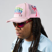Person wearing a pink cap with colorful designs and sunglasses, against a plain background